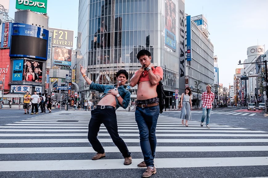 A busy Japanese city with two young men posing on a zebra crossing