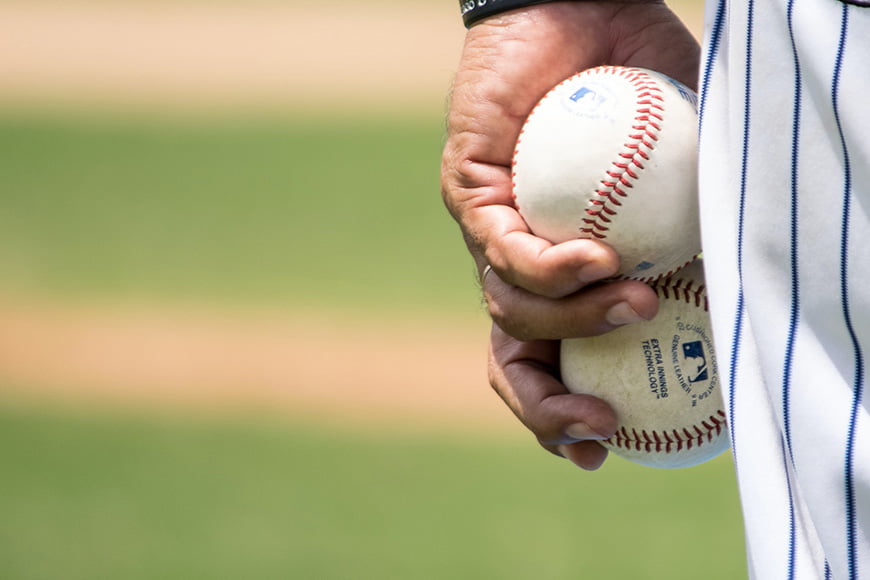 Close up of a hand holding two baseballs