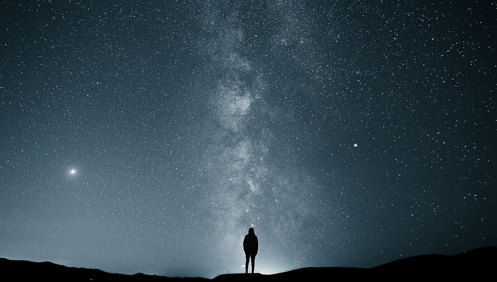 One person standing under a moody night sky