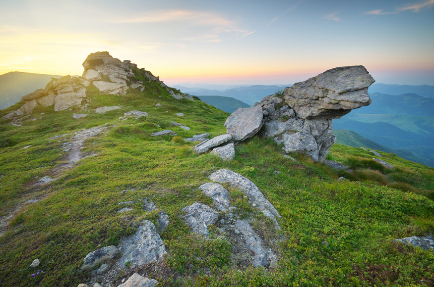 Image of a rocky mountain top with lush green cover and one rock jutting out 