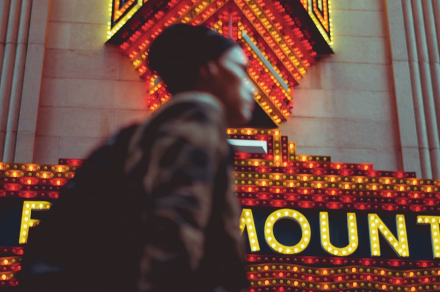 City photography - man walking past a large brightly lit sign