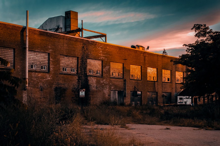 Photo of an old factory building with a moody light and pink and grey clouds