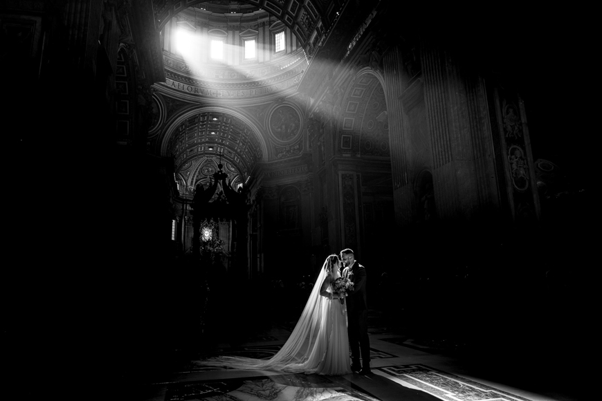 A bride and groom standing in the light of the sun in a church.