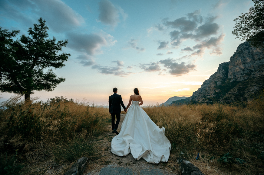 A bride and groom walking down a path at sunset.