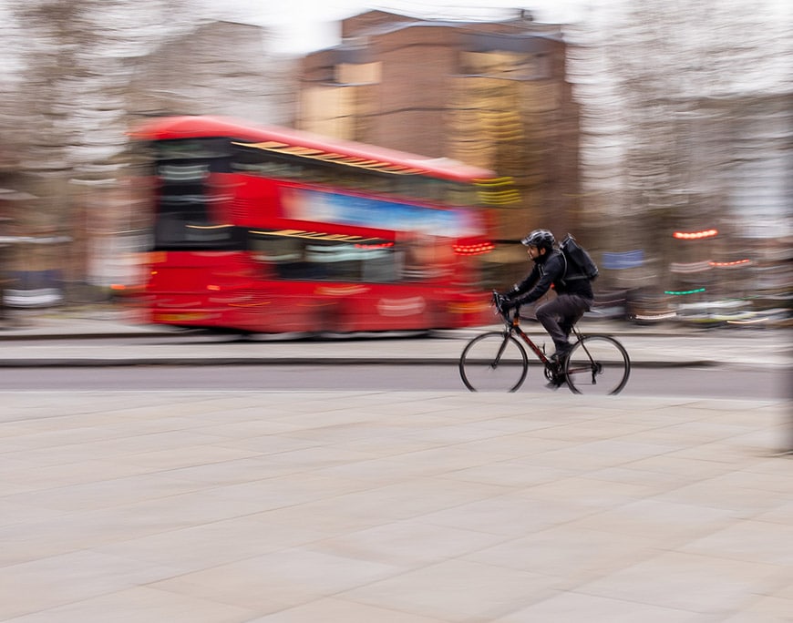 Man riding a bicycle with red bus blurred in background