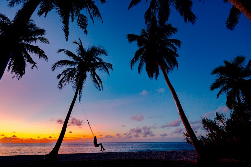 Silhouette of girl on a swing with palm trees