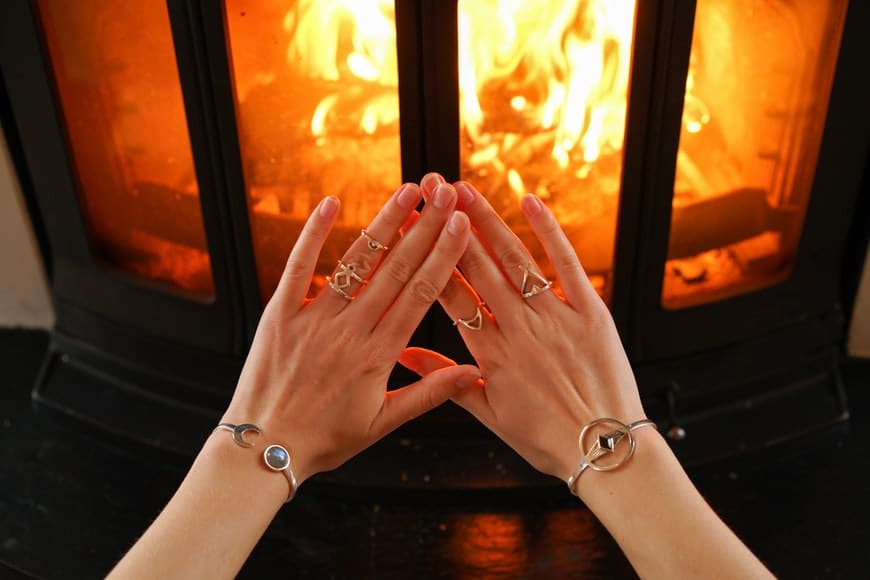 Woman with jewellery warming hands in front of fire