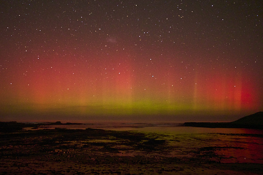 a bright green and red aurora over a body of water.