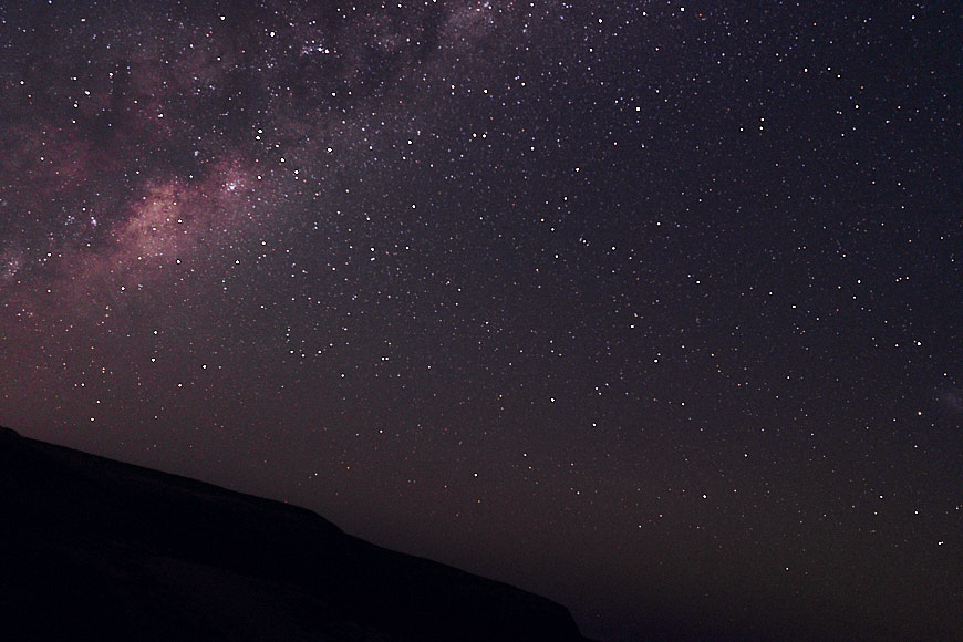 a person standing on a hill looking up at the stars.