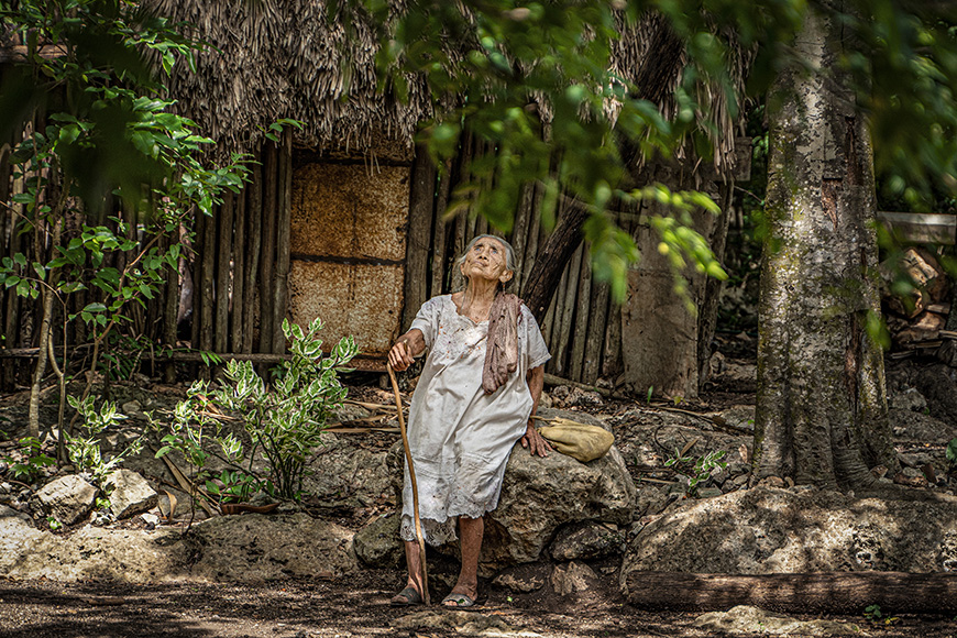 a woman in a white dress standing in front of a hut.