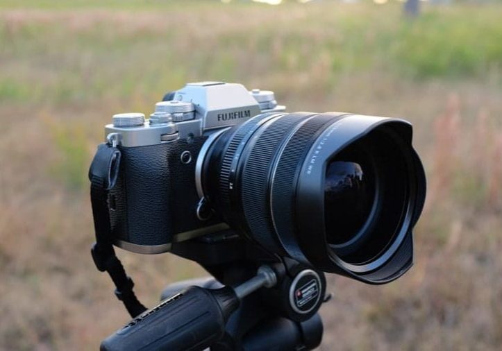 a fuji xt5 camera attached to a tripod in a field.