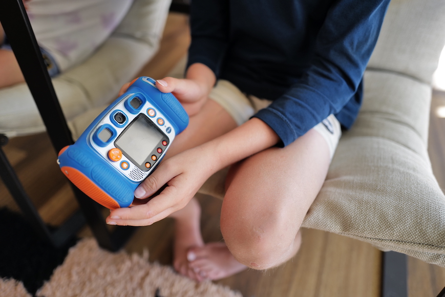 a young boy sitting on a chair holding a blue and orange cell phone.