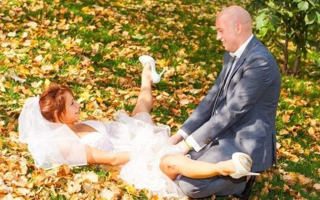 a bride and groom sitting on the ground in the leaves.