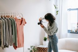 a woman taking a picture of clothes hanging on a rack.