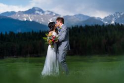 a bride and groom kissing in a field at a wedding with mountains in the background.