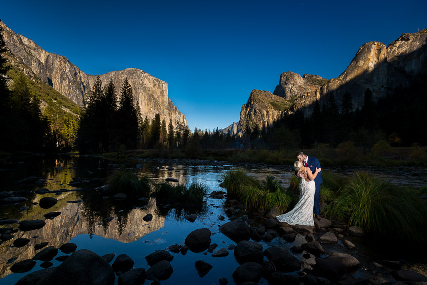 a bride and groom standing in front of a mountain lake.