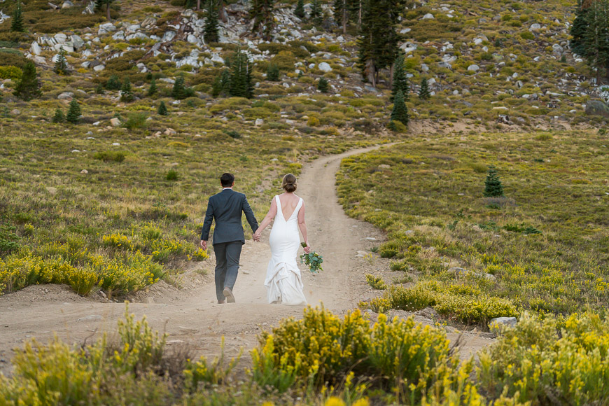 a bride and groom walking down a dirt road.
