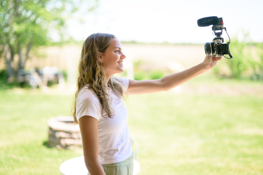 a woman holding a video camera in her hand with the Joby Wavo Plus mic.