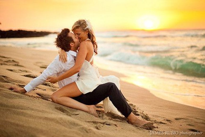a man and woman sitting on the beach kissing.