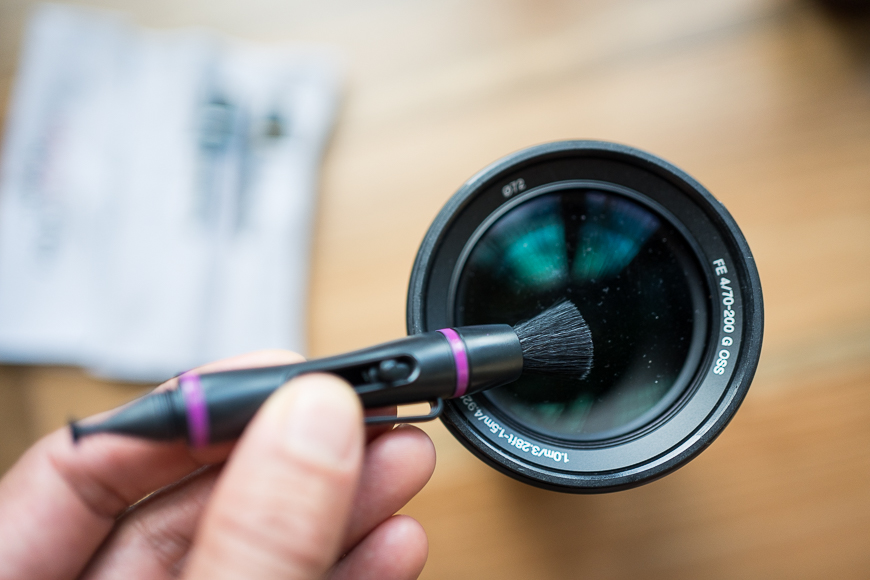 a person holding a camera lens with a lenspen brush in it.