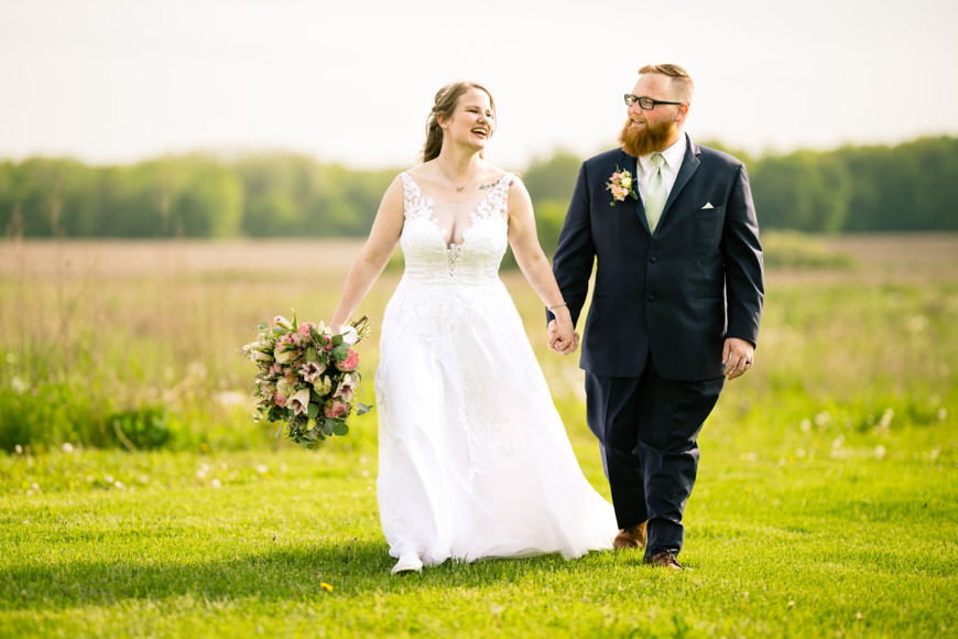 a bride and groom walking through a field.