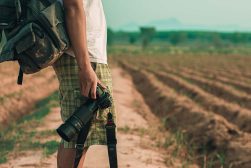 a man with a camera and a backpack on a dirt road.
