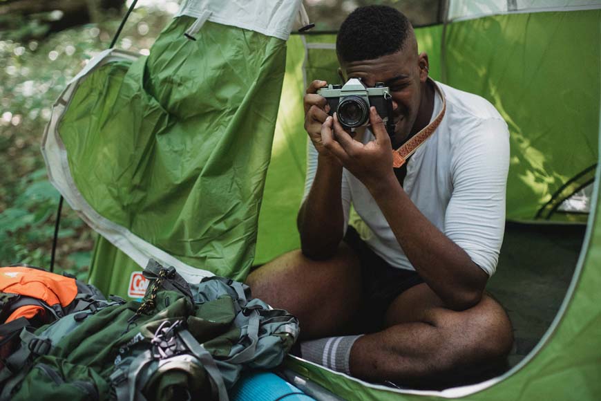 a man sitting inside of a tent holding a camera.