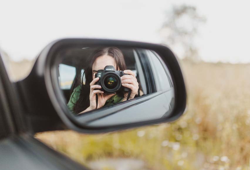 a woman taking a picture of herself in a car mirror.