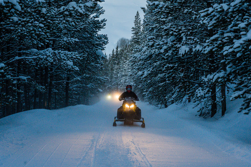 a person riding a snowmobile down a snow covered road.