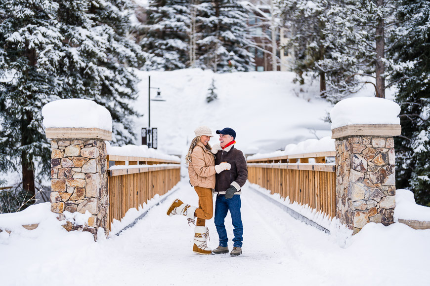 a man and woman standing on a bridge in the snow.
