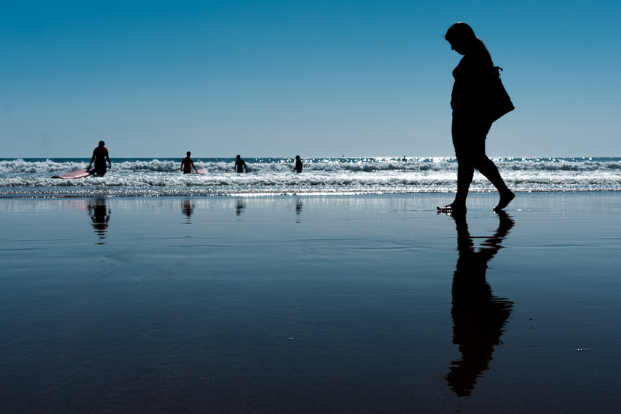 a woman walking along a beach next to the ocean.