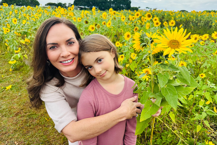 a woman and a little girl standing in a field of sunflowers.