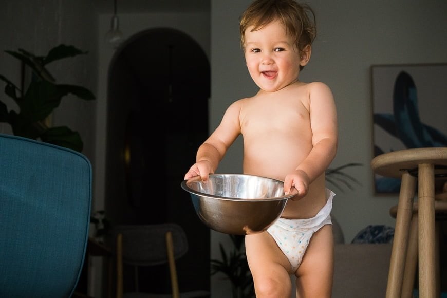 a baby in a diaper holding a metal bowl.
