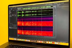 A macbook screen showing the waveform view of an audio file in adobe audition with a yellow background