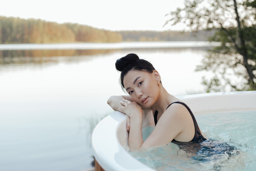 a woman sitting in a hot tub next to a lake.