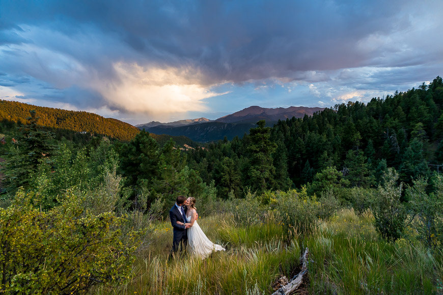 a bride and groom standing in a field with mountains in the background.