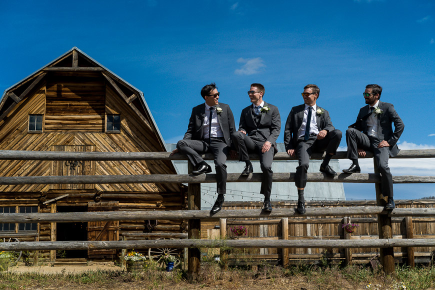 a group of men sitting on top of a wooden fence.