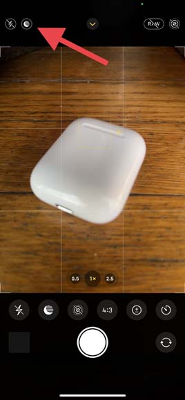 screenshot of the iPhone camera showing an airpod case on a wooden table with a red arrow pointing to the night mode settings.