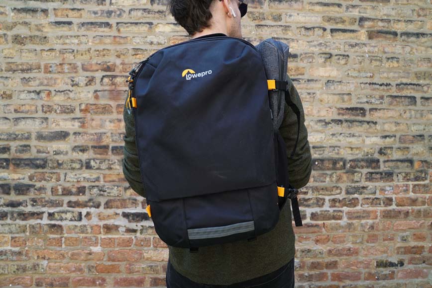a man with a backpack on his back standing in front of a brick wall.