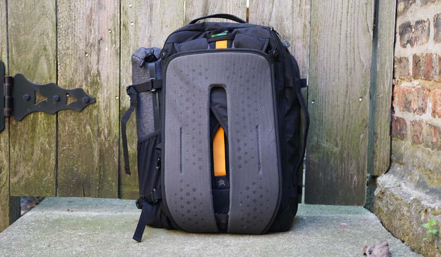 a backpack sitting on the ground in front of a wooden fence.