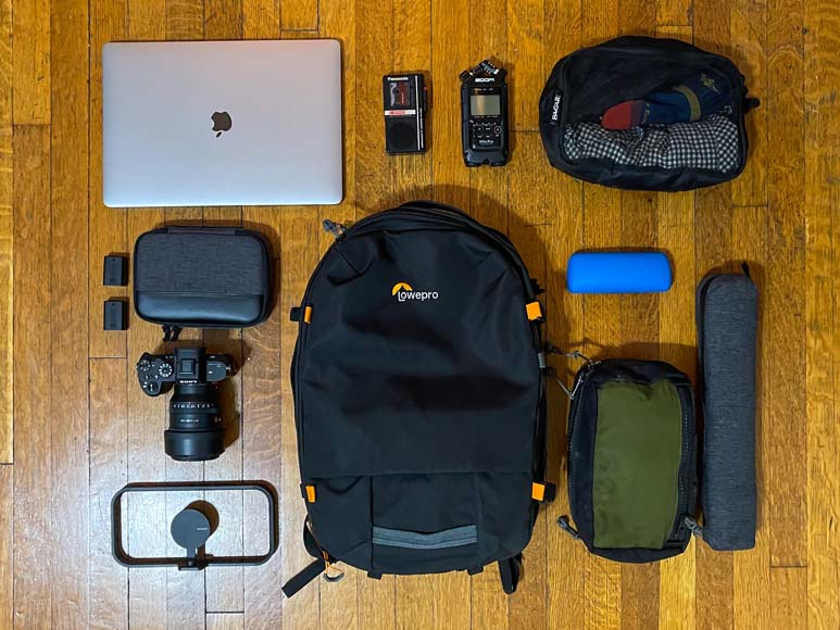 a backpack, a camera, a laptop, and other items laid out on a wooden floor