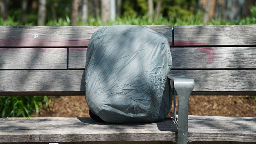 a backpack with a rain cover sitting on top of a wooden bench.