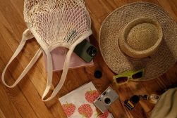 a hat, sunglasses, camera, and other items on a wooden floor.