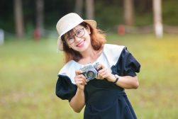 a woman in a dress and hat holding a camera.