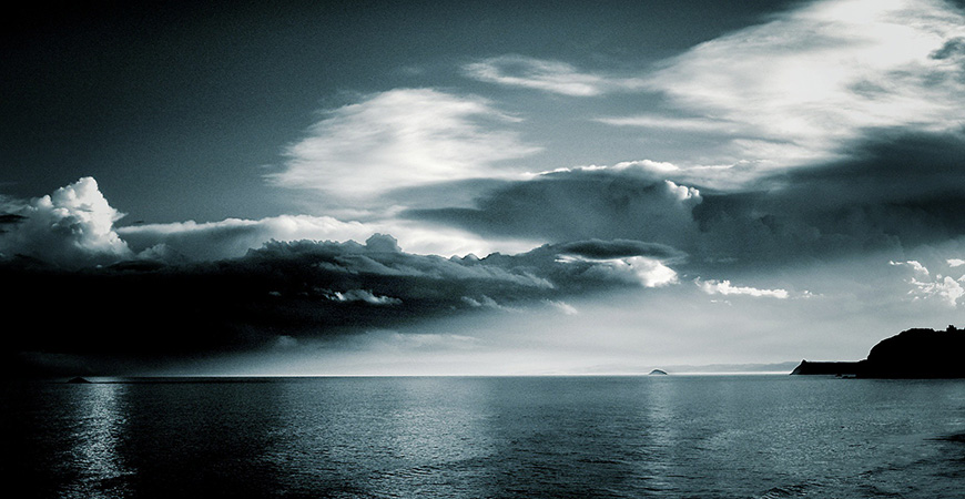 a black and white photo of a cloudy sky over a body of water.