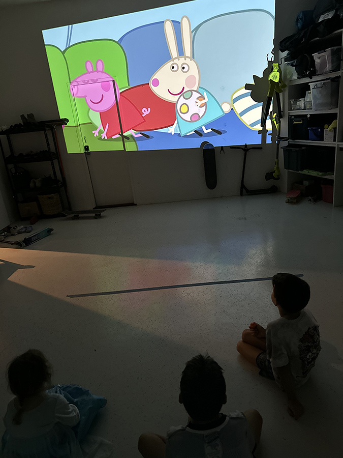 a group of children sitting on the floor in front of a large projector screen.