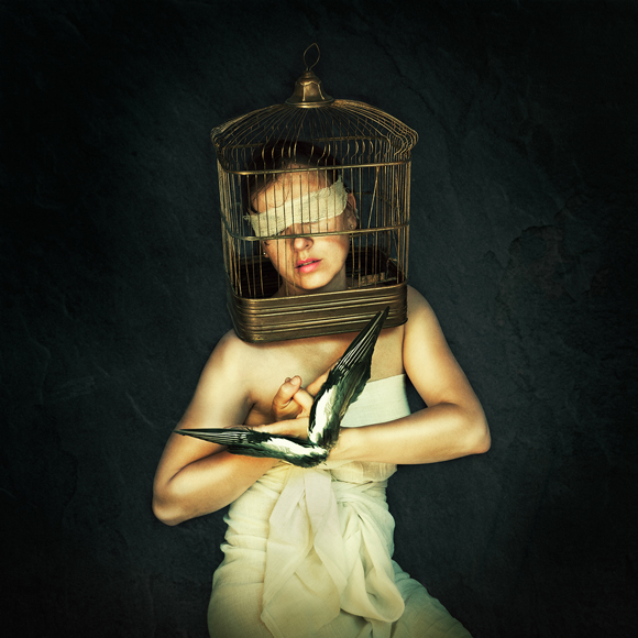 a woman in a white dress holding a bird in a cage.