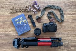 a camera, a book, a camera strap, and other items laid out on.