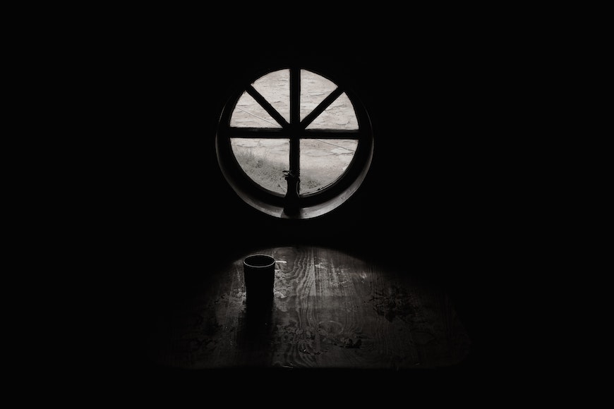 a dark room with a round window and a cup.