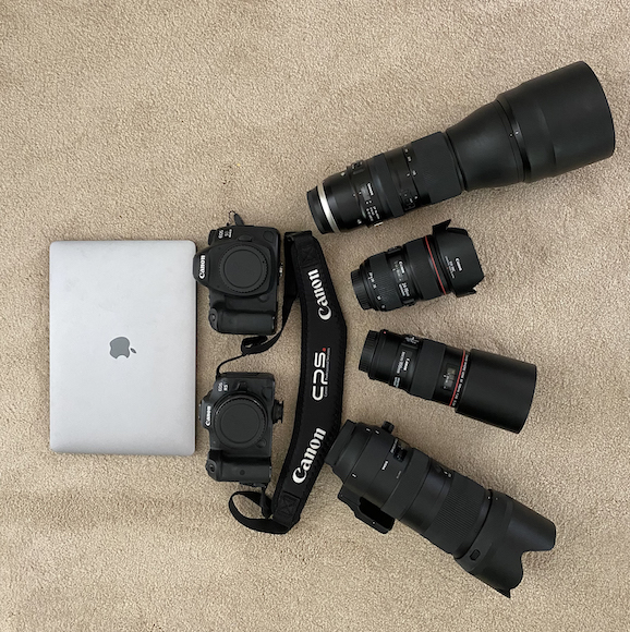 a camera, a laptop, a camera lens, and other items are laid out.
